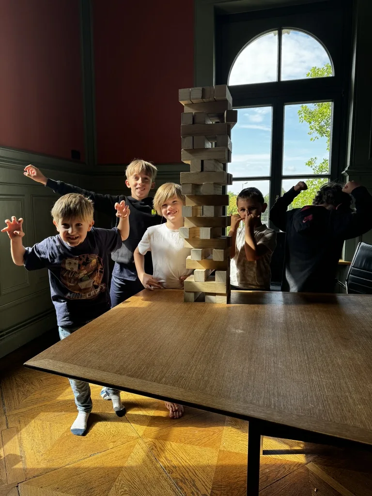 Eine Kindergruppe steht hinter einem gemeinsam gebauten hohen Turm aus Holzklötzen.