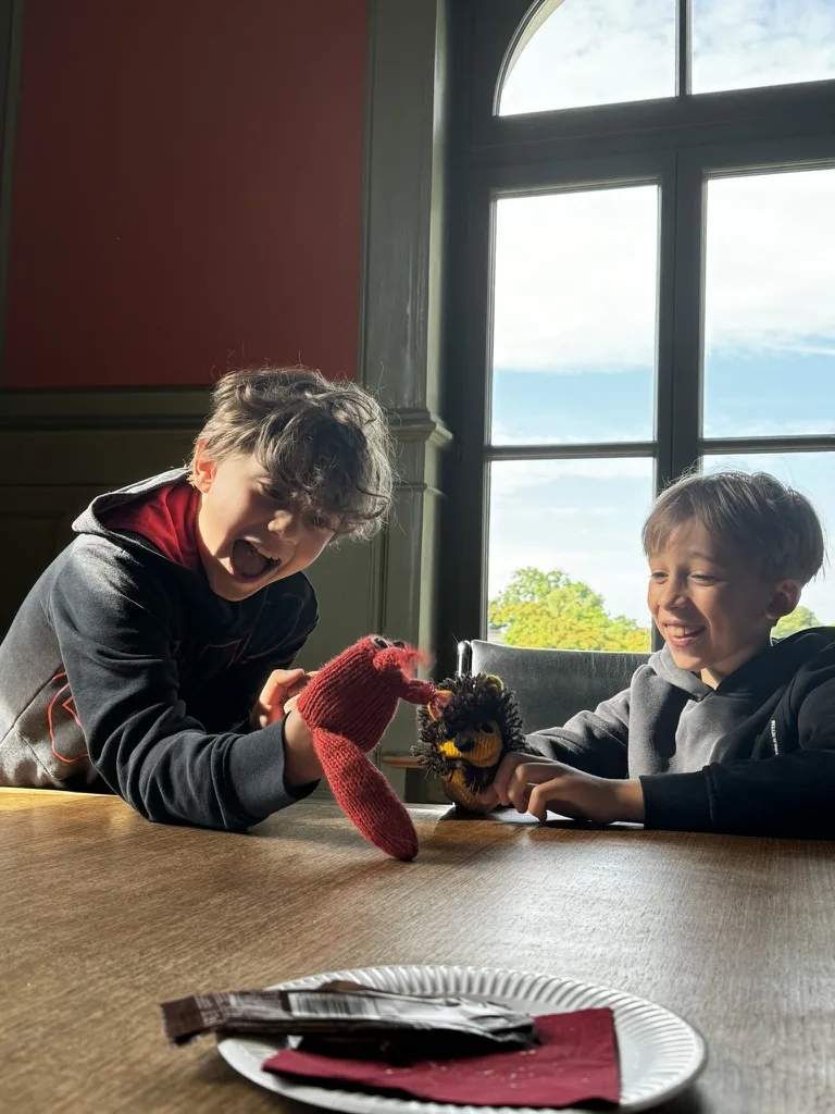Zwei Kinder beschäftigen sich gemeinsam mit Handpuppen am Tisch.